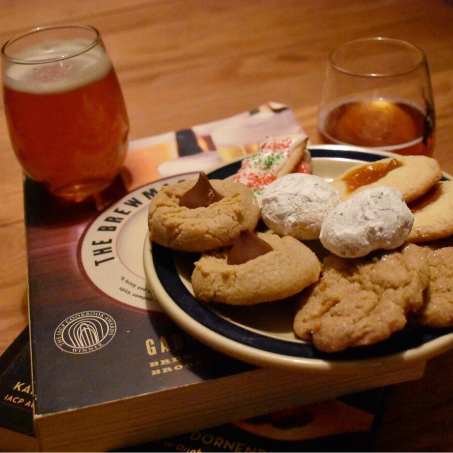 A photo of Christmas cookies (snowball cookies, apricot thumbprint cookies, orange gingerbread cookies, sugar cookies with buttercream frosting, and peanut butter blossom cookies) paired with craft beer.